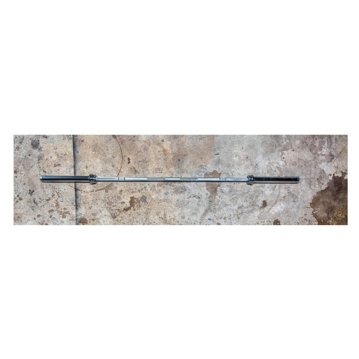 York Barbell 7’ USA Power Bar full view lying on a warehouse floor, showcasing its 29mm shaft, satin chrome finish, and high-quality U.S. steel construction.