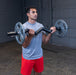 Close-up of a male athlete performing a standing EZ curl with the Body-Solid FAT CURL BAR OB48F, showcasing the thick 2" grip and intense bicep engagement during the exercise.

