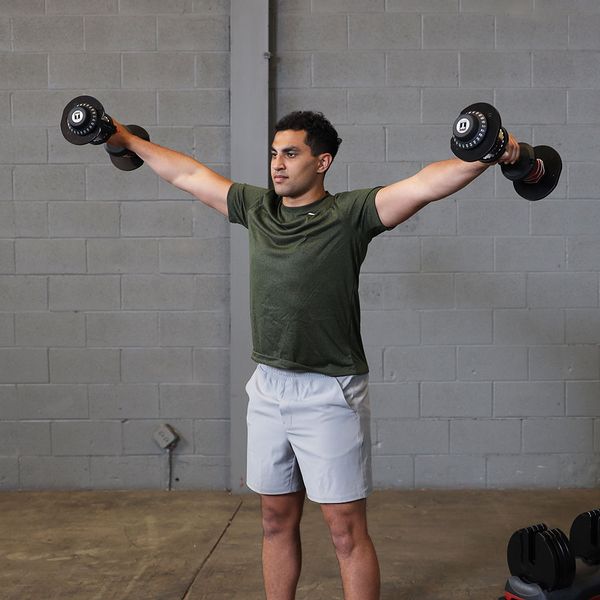 Person performing a lateral raise with Body-Solid Tools SDBX132 Adjustable Dumbbells, lifting the dumbbells to shoulder height with arms slightly bent.